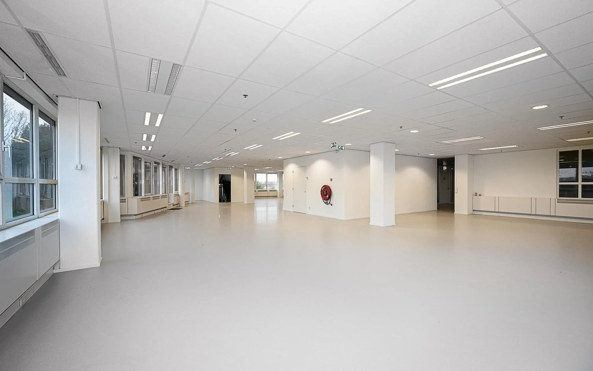 Ruime, lege kantoorruimte in Rivium Quadrant met witte muren, systeemplafond en grote ramen.